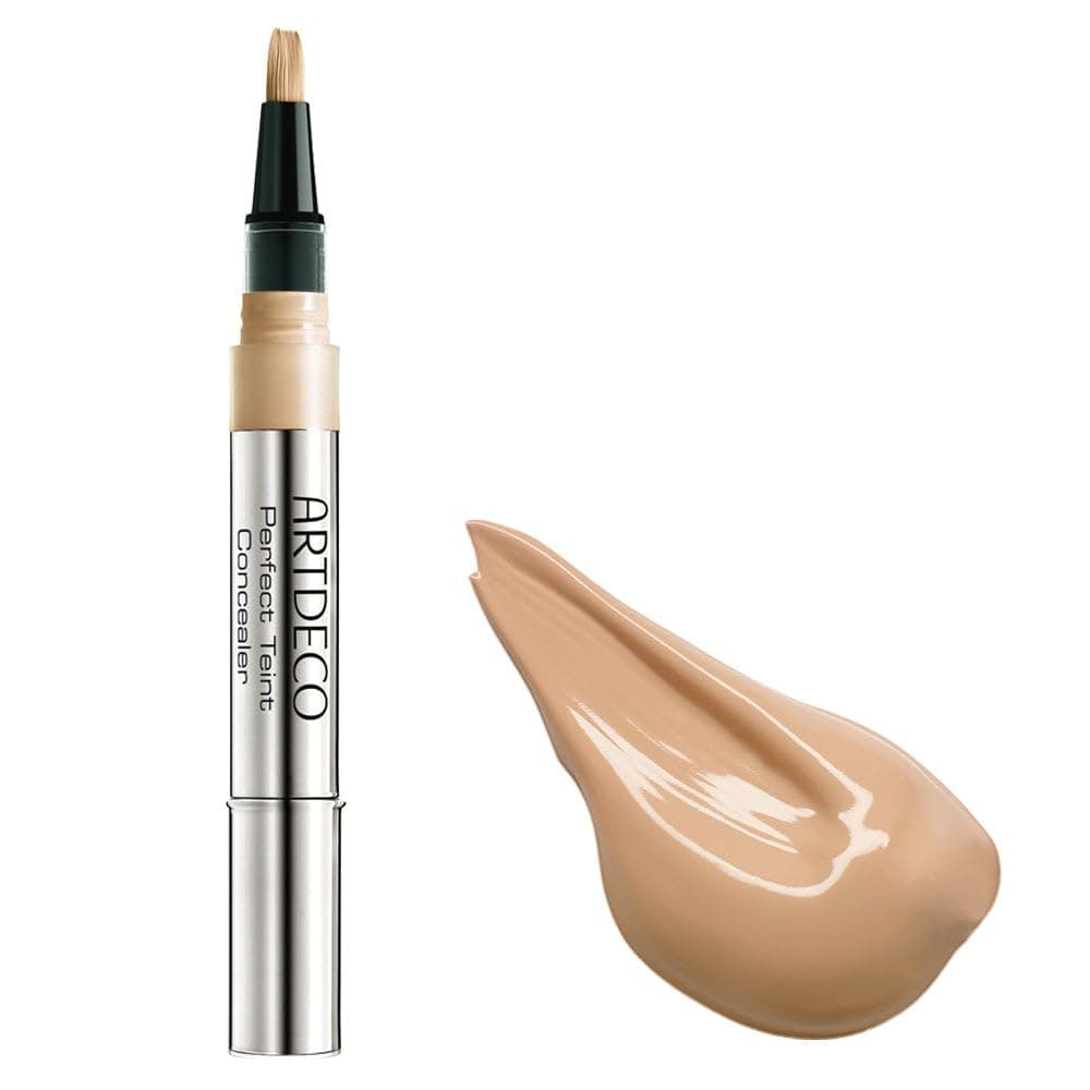Silberner Concealer-Stift mit dunkelgrüner Kappe und Pinselspitze, daneben ein beigefarbener Tropfen des Produkts
