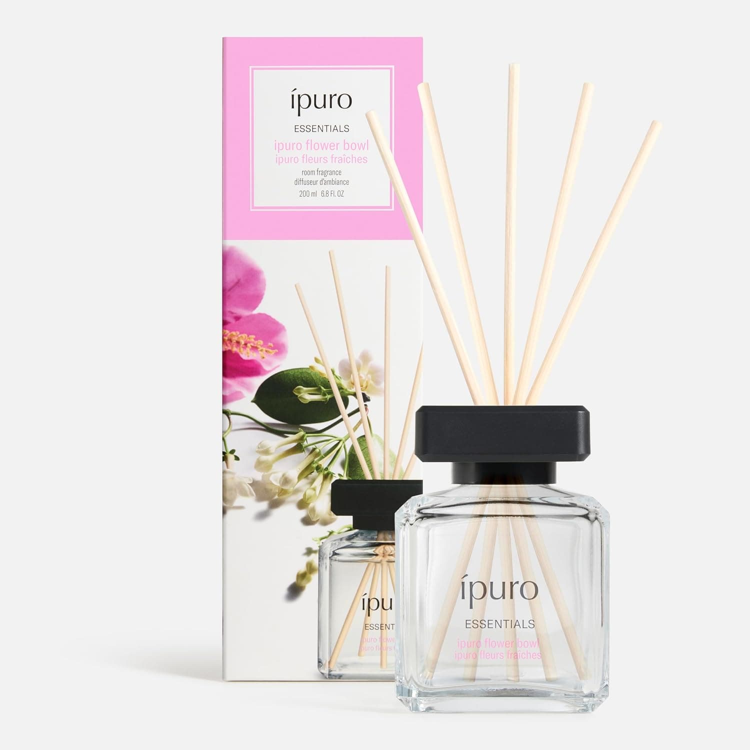 Farbloser Glasflakon mit schwarzem Deckel und fünf hellen Duftstäbchen, daneben die rosa-weiße Verpackung mit Blüten und der Aufschrift ipuro Essentials, ipuro flower bowl, 200 ml