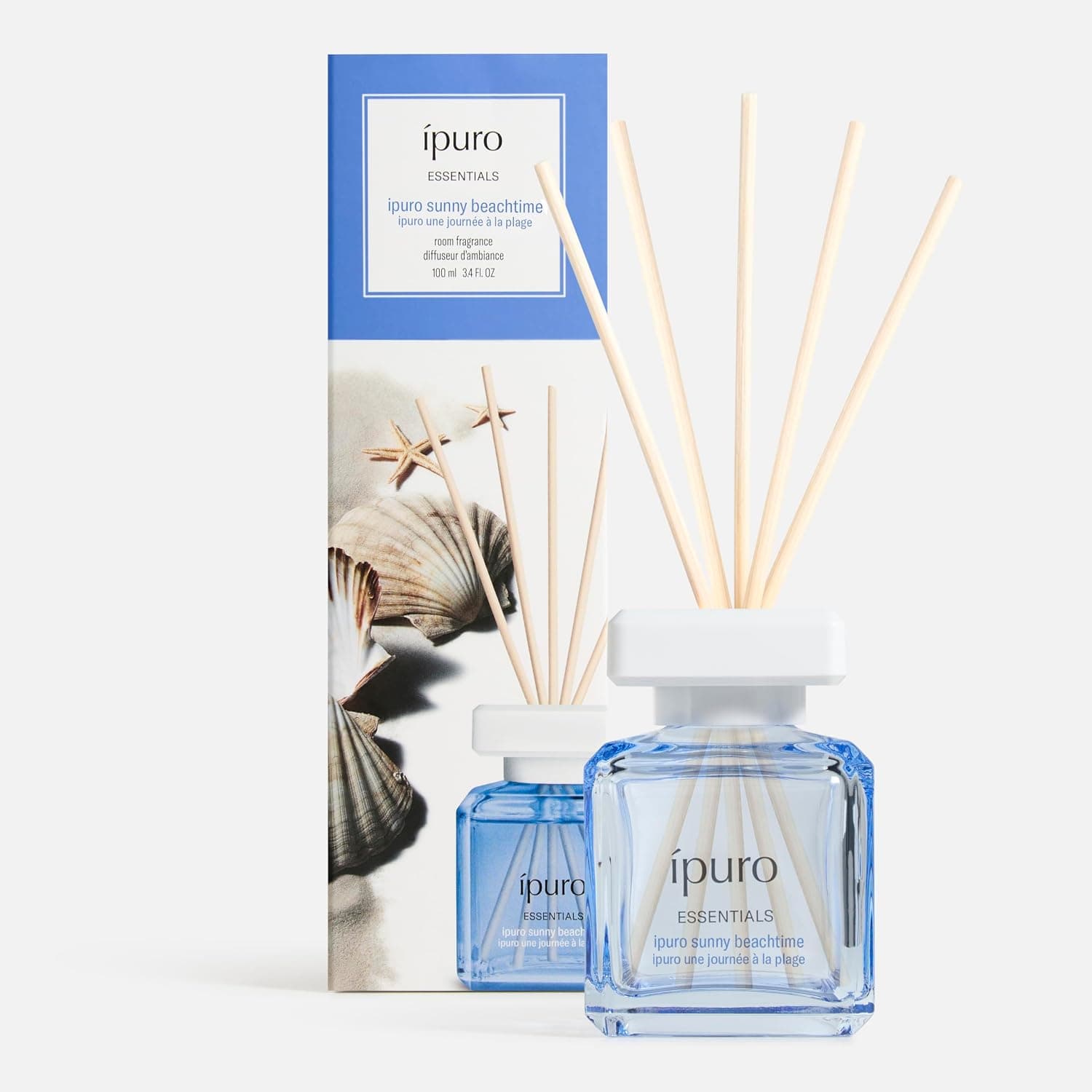Blauer Glasflakon mit weißem Deckel und fünf hellen Duftstäbchen, daneben die blau-weiße Verpackung mit Muscheln und Seesternen und der Aufschrift ipuro Essentials, ipuro sunny beachtime, 100 ml