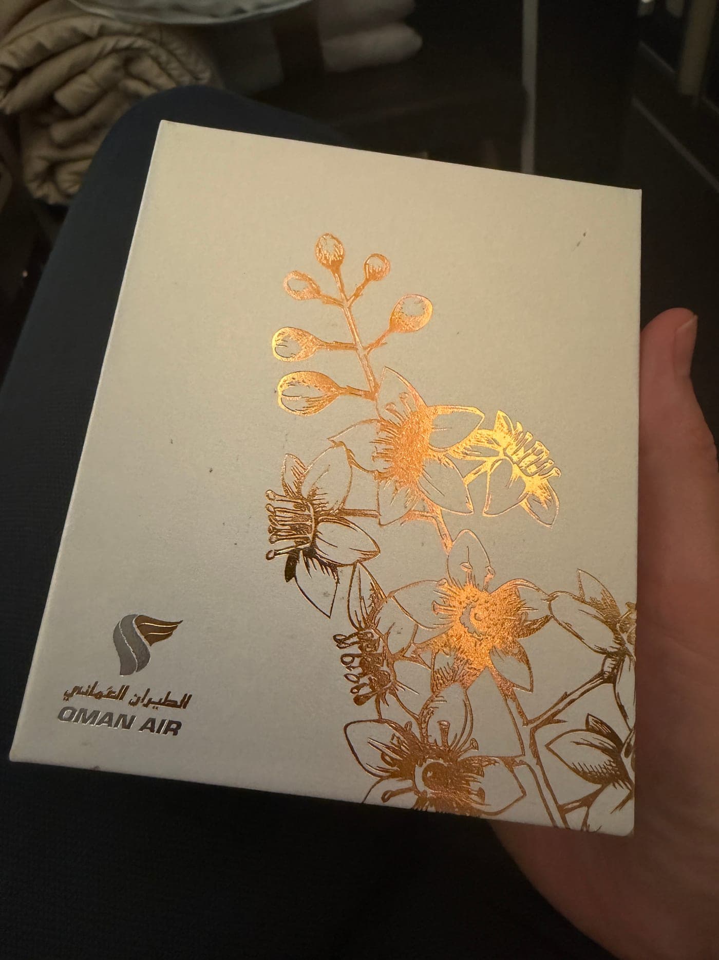Amenity-Schachtel von Oman Air mit goldener Blütenprägung, in der Hand gehalten