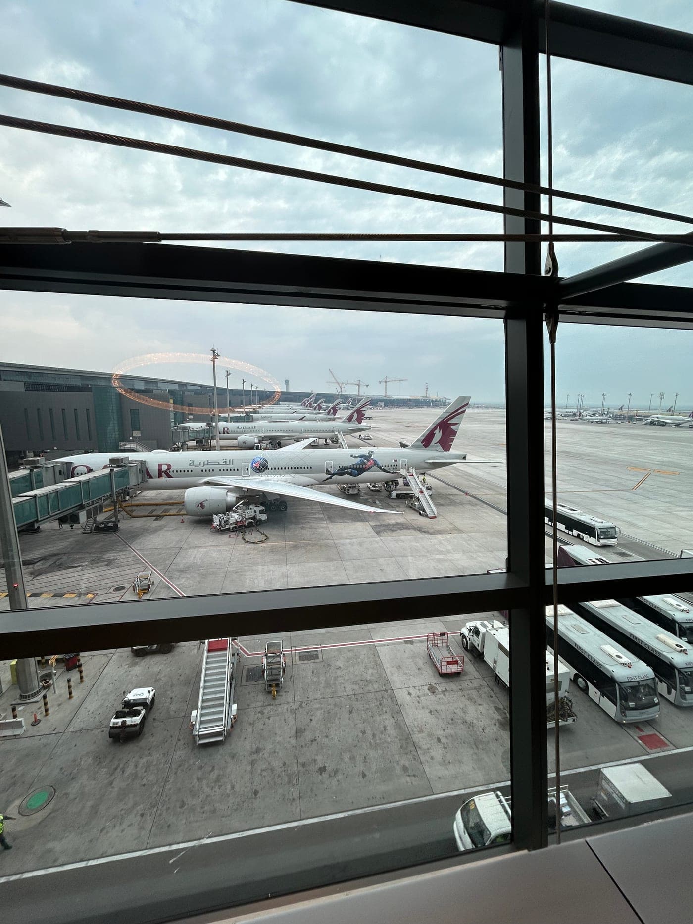 Blick aus der Al Safwa Lounge auf das Vorfeld in Doha, Maschinen von Qatar Airways am Gate und davor Busse mit der Aufschrift First Class